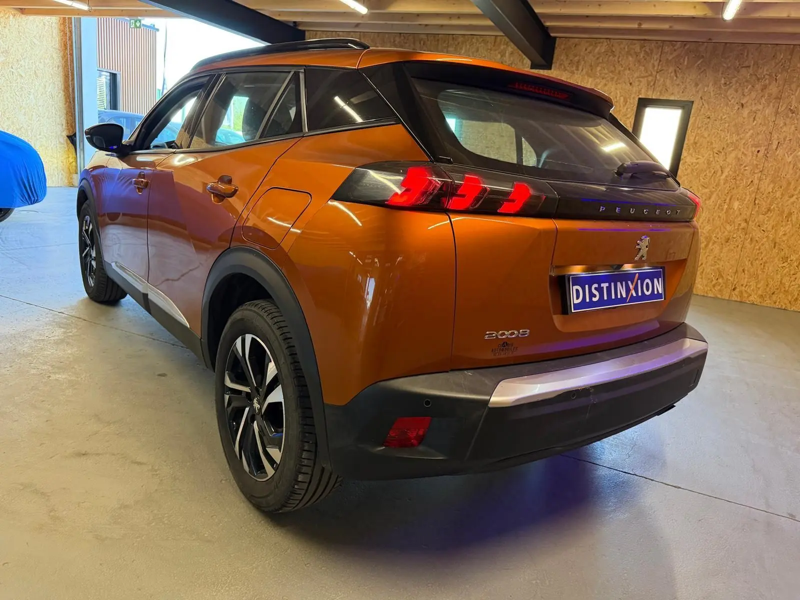 Vue 3/4 arrière droite d'un Peugeot 2008 orange métallisé avec feux arrière LED en forme de griffes et jantes alliage bi-ton.