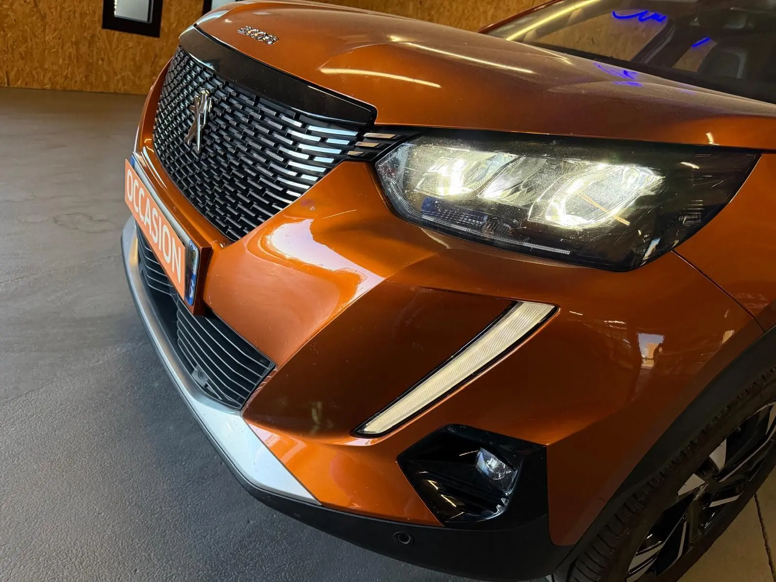 Vue 3/4 avant droit d’un Peugeot 2008 orange métallisé avec phares LED allumés et calandre noire distinctive.