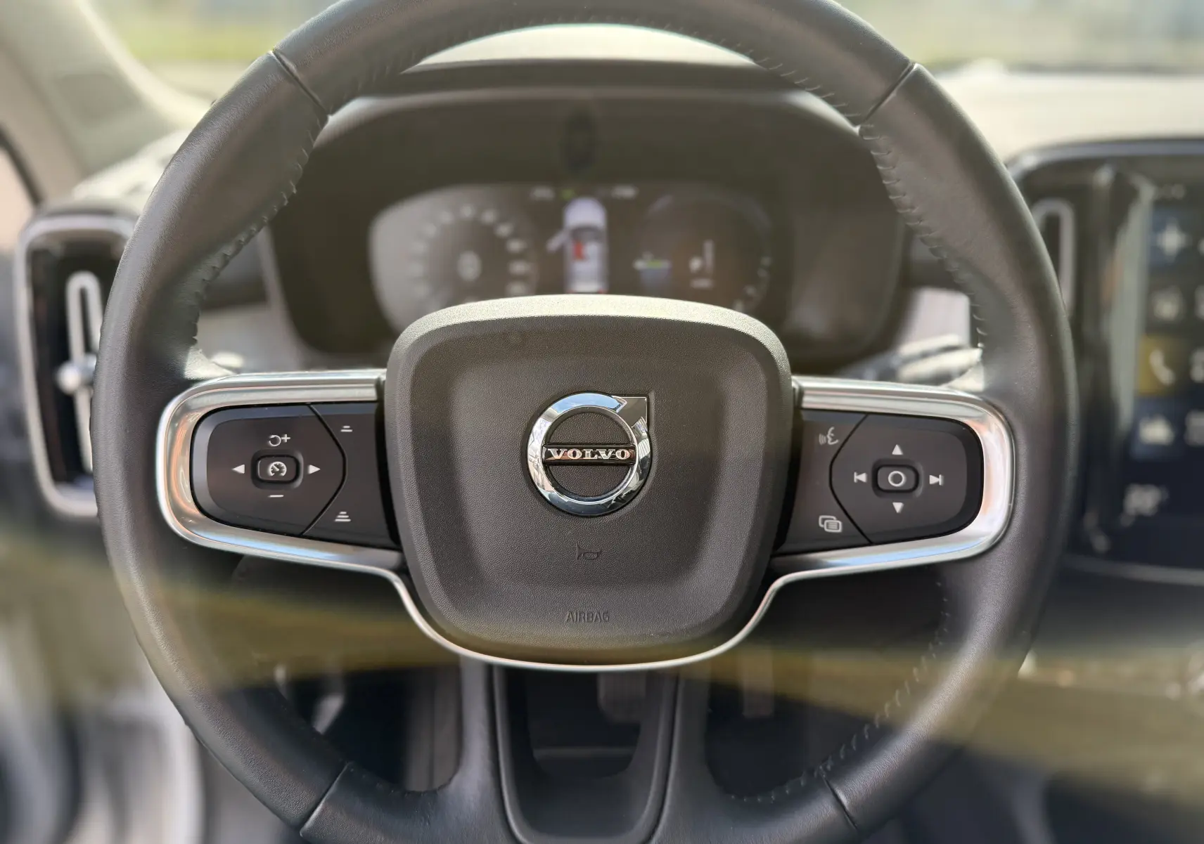 Volant noir avec logo Volvo au centre, vue frontale du poste de conduite du XC40 hybride rechargeable blanc cristal métal.