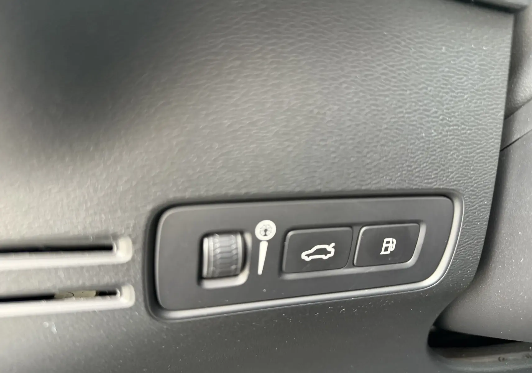 Gros plan sur les commandes d’ouverture du coffre et de la trappe à carburant dans un Volvo XC40 blanc Crystal Metal hybride rechargeable.