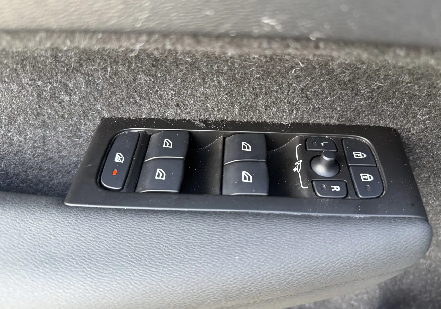 Gros plan sur les commandes de lève-vitres et rétroviseurs sur la porte intérieure d’un Volvo XC40 blanc.
