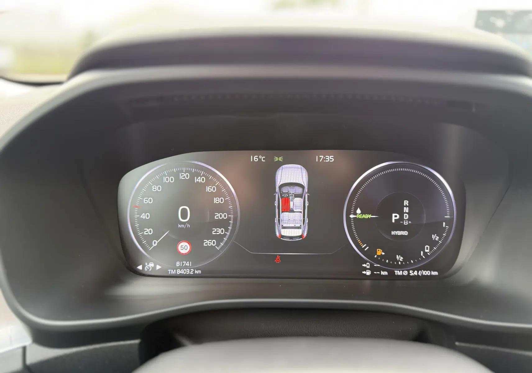 Tableau de bord numérique du Volvo XC40 blanc, affichant vitesse, mode hybride et état des portes à 17h35.