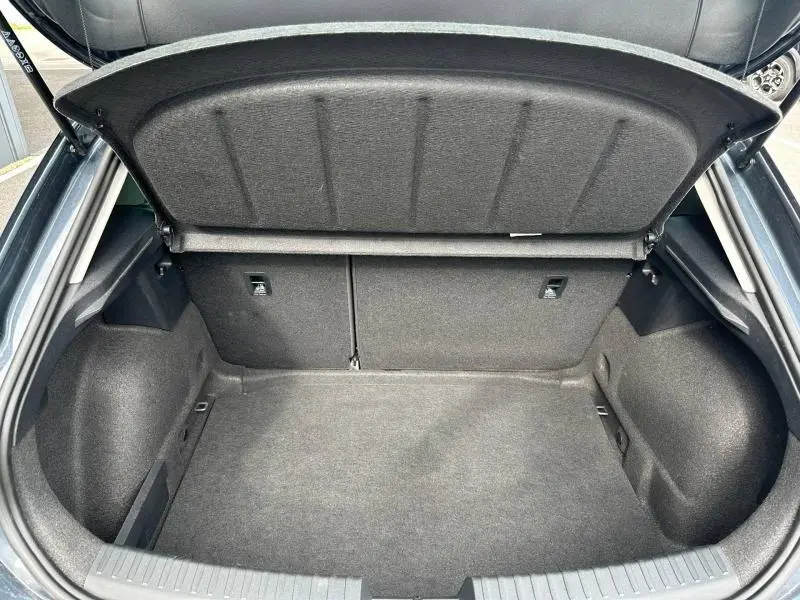 Coffre ouvert vu de l'arrière d'une SEAT LEON 2025 noir Minuit Métallisée, espace de rangement vide et tapis gris.