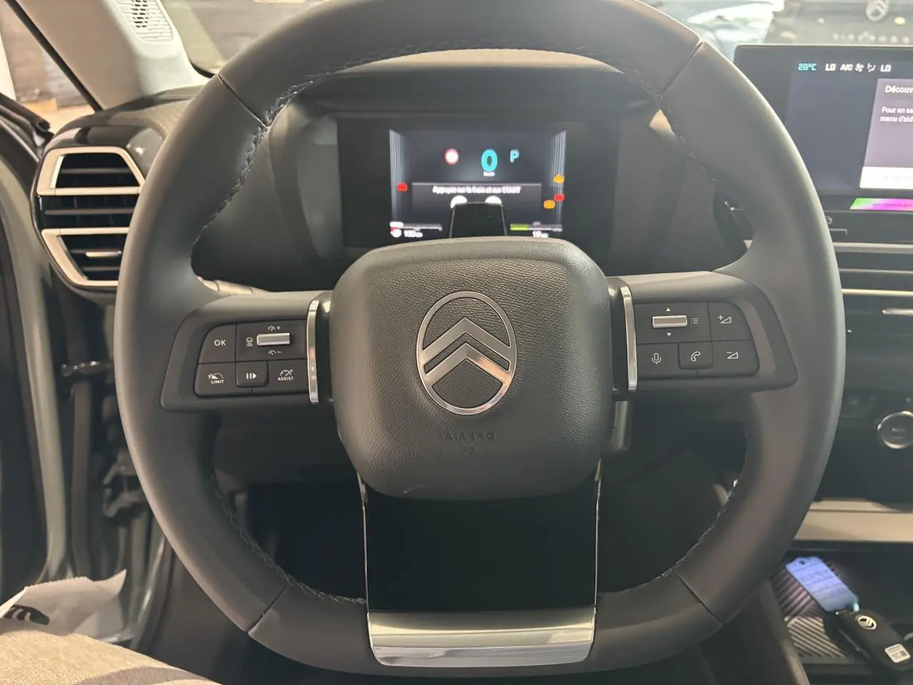 Vue rapprochée du volant cuir noir multifonctions avec logo Citroën au centre et tableau de bord numérique en arrière-plan.