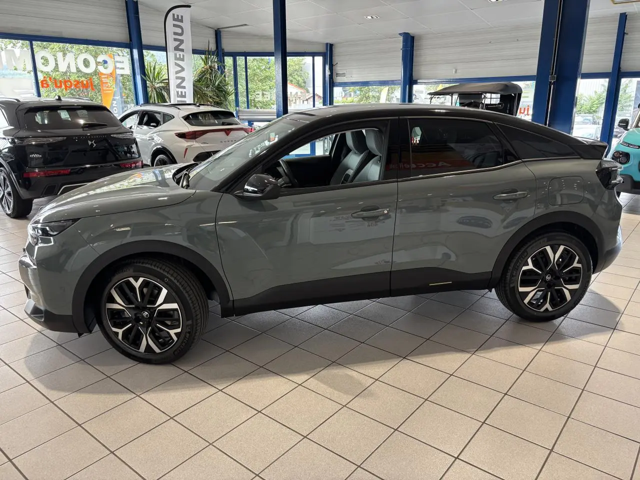 Profil côté gauche d'une Citroën C4 2026 vert Manhattan avec toit noir Perla Nera en showroom.