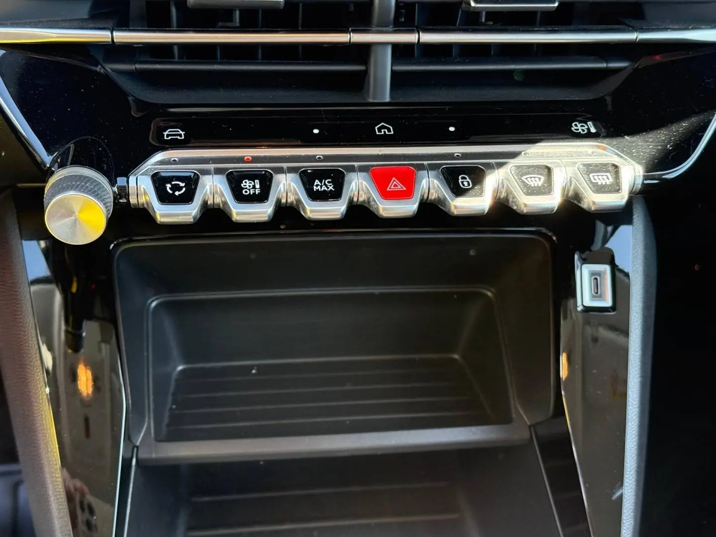 Gros plan sur la console centrale de la Peugeot 208 1.2 Hybrid 110ch Style, boutons argentés et rouge sur fond noir brillant.