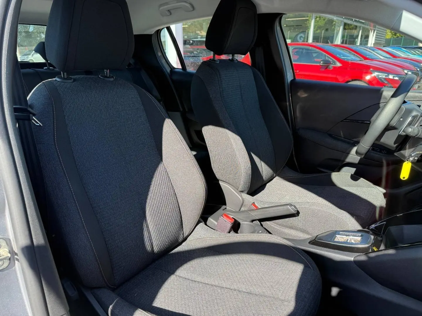 Vue intérieure des sièges avant en tissu gris RENZO avec surpiqûres Orange Sunrise d'une Peugeot 208 1.2 Hybrid 2025.