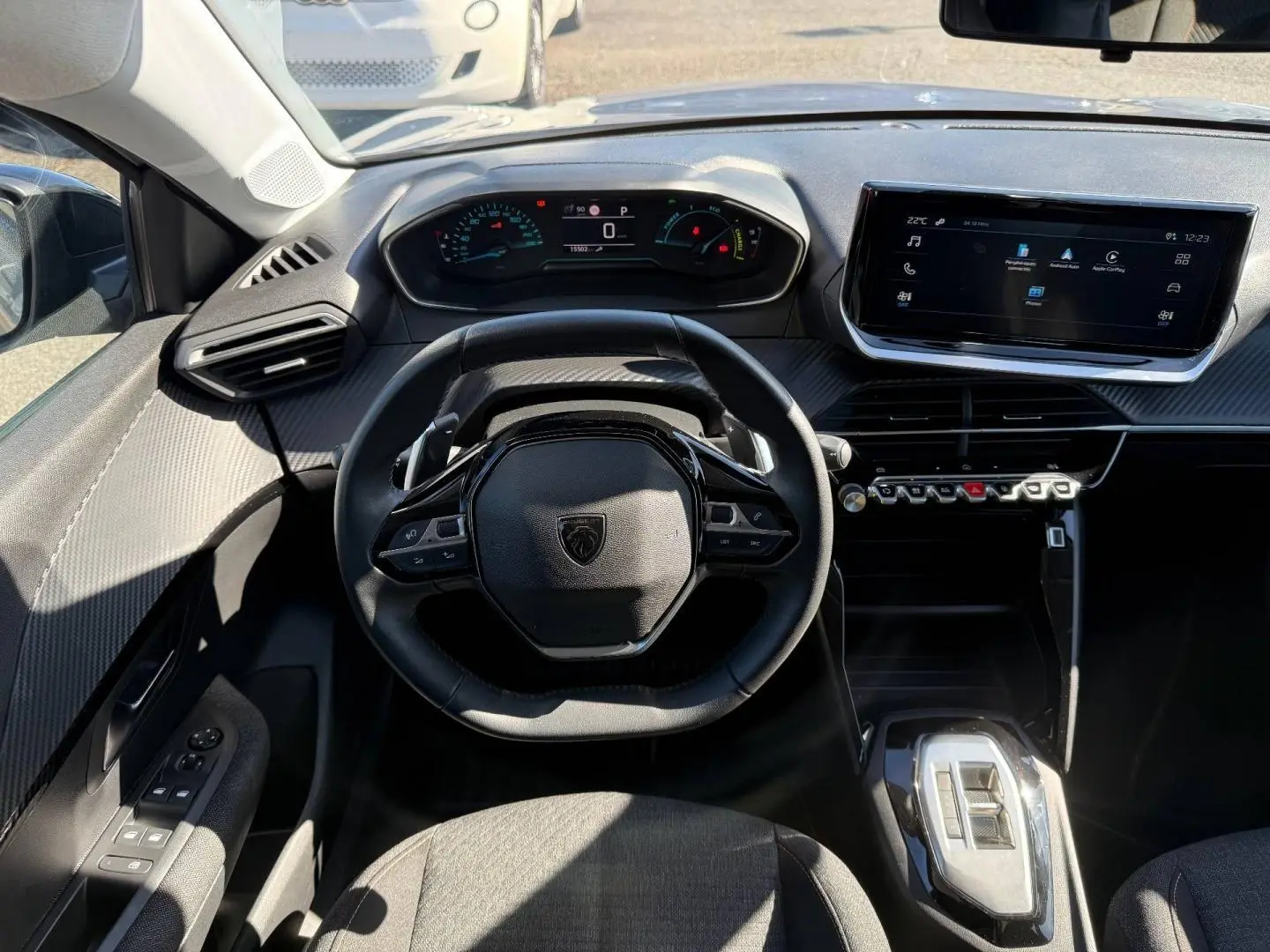 Vue intérieure frontale du poste de conduite de la Peugeot 208 gris Artense, avec volant compact et écran tactile central.