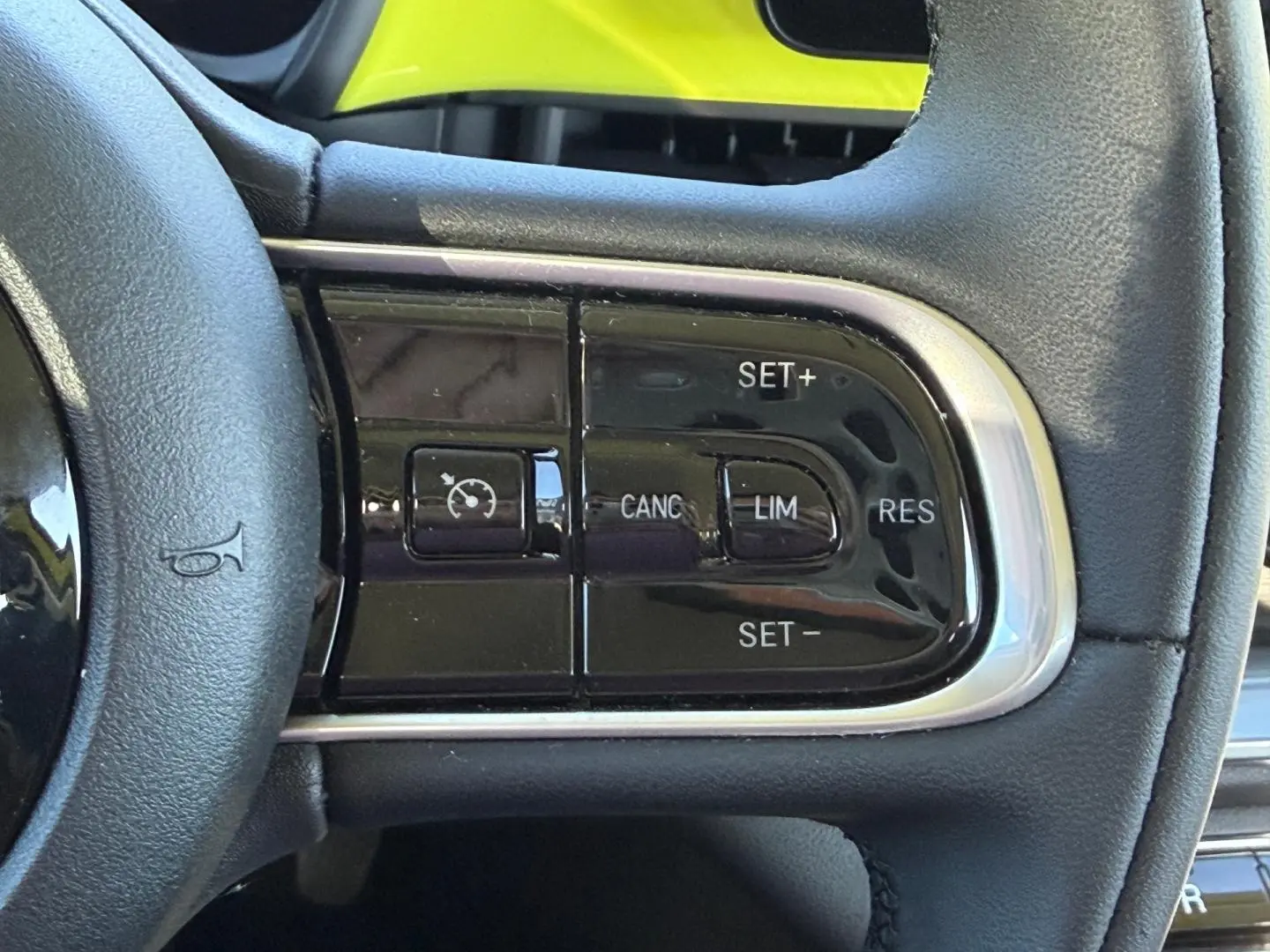 Gros plan sur les commandes de régulateur de vitesse au volant noir de la FIAT 500 e Ocean Green métal 2024.