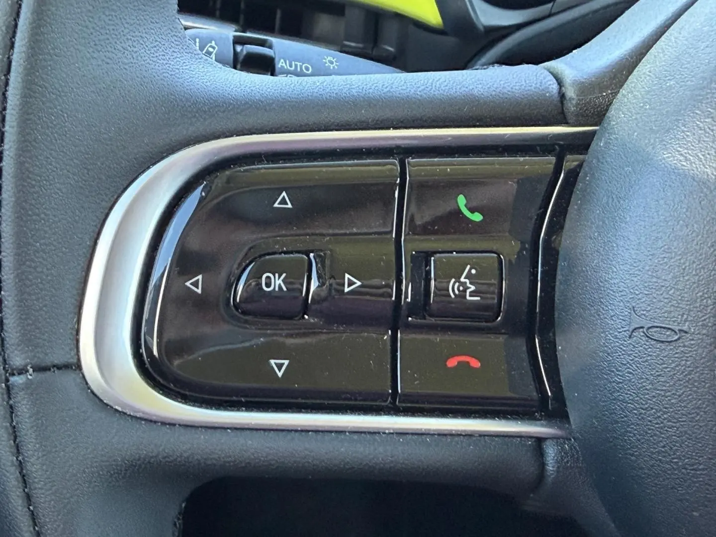 Gros plan sur les commandes multifonctions noires du volant côté gauche de la Fiat 500 e 95ch Ocean Green métal.