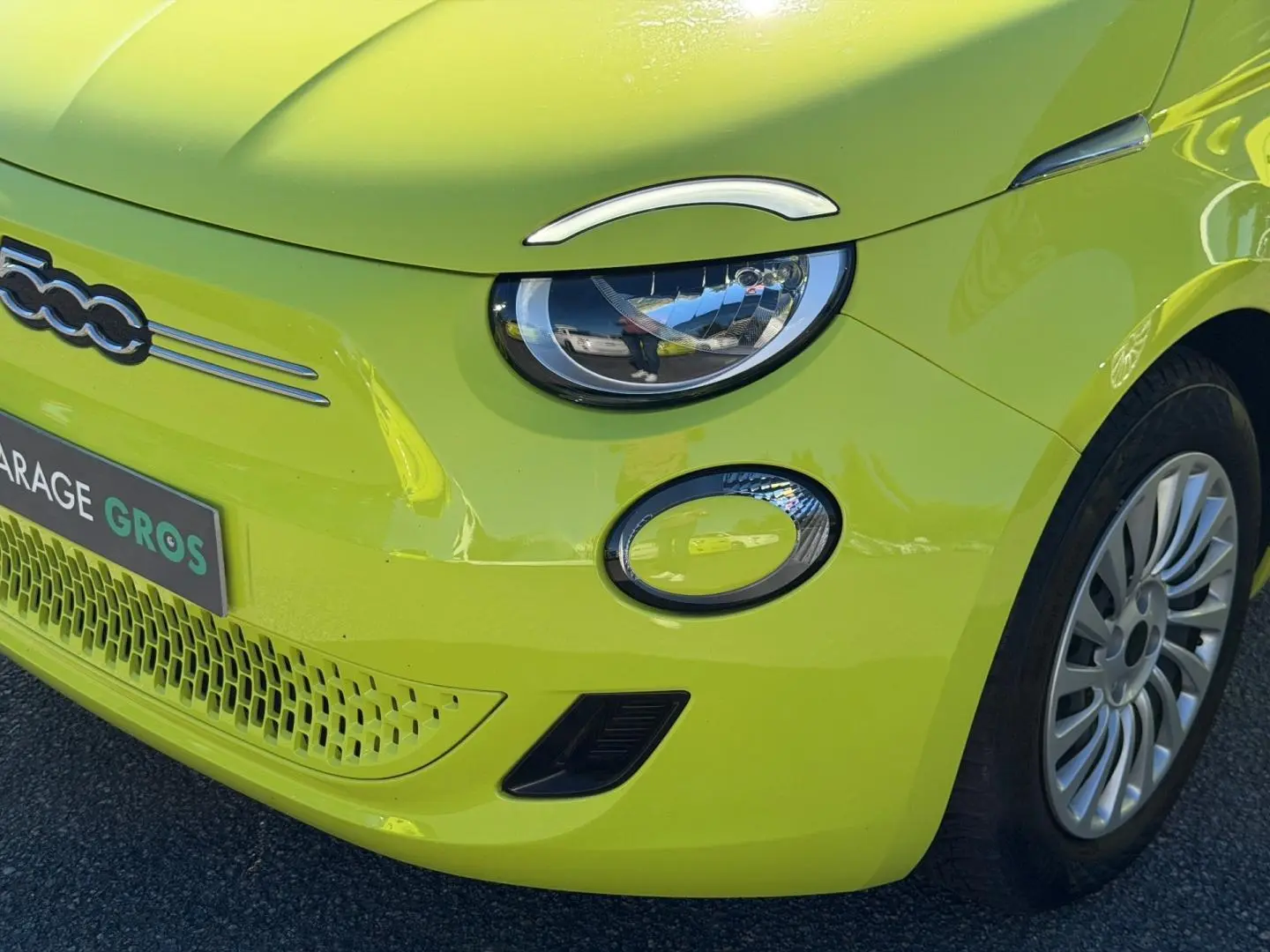 Gros plan sur l'avant droit de la Fiat 500 électrique Ocean Green métal avec phares ronds et jante argentée.
