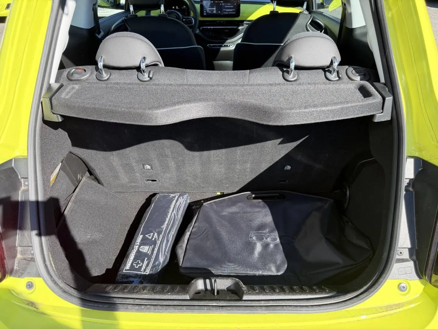 Coffre ouvert vu de l'arrière d'une FIAT 500 électrique Ocean Green métal avec accessoires de rangement noirs.
