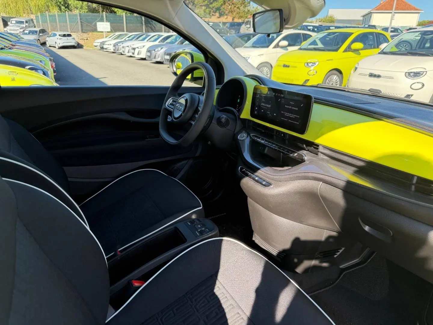 Vue intérieure côté conducteur de la Fiat 500 e 95ch Ocean Green avec tableau de bord jaune vif et sièges noirs.
