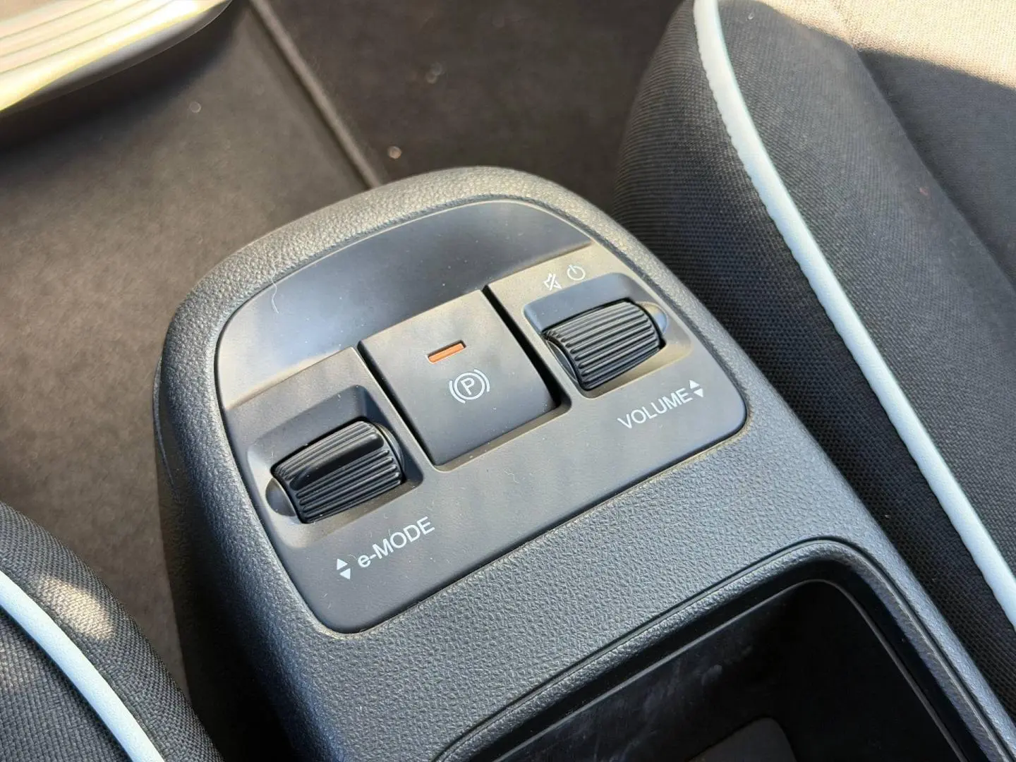 Gros plan sur la console centrale de la Fiat 500 e 95ch Pack Confort MY23 avec commandes e-Mode, frein à main électrique et réglage volume.