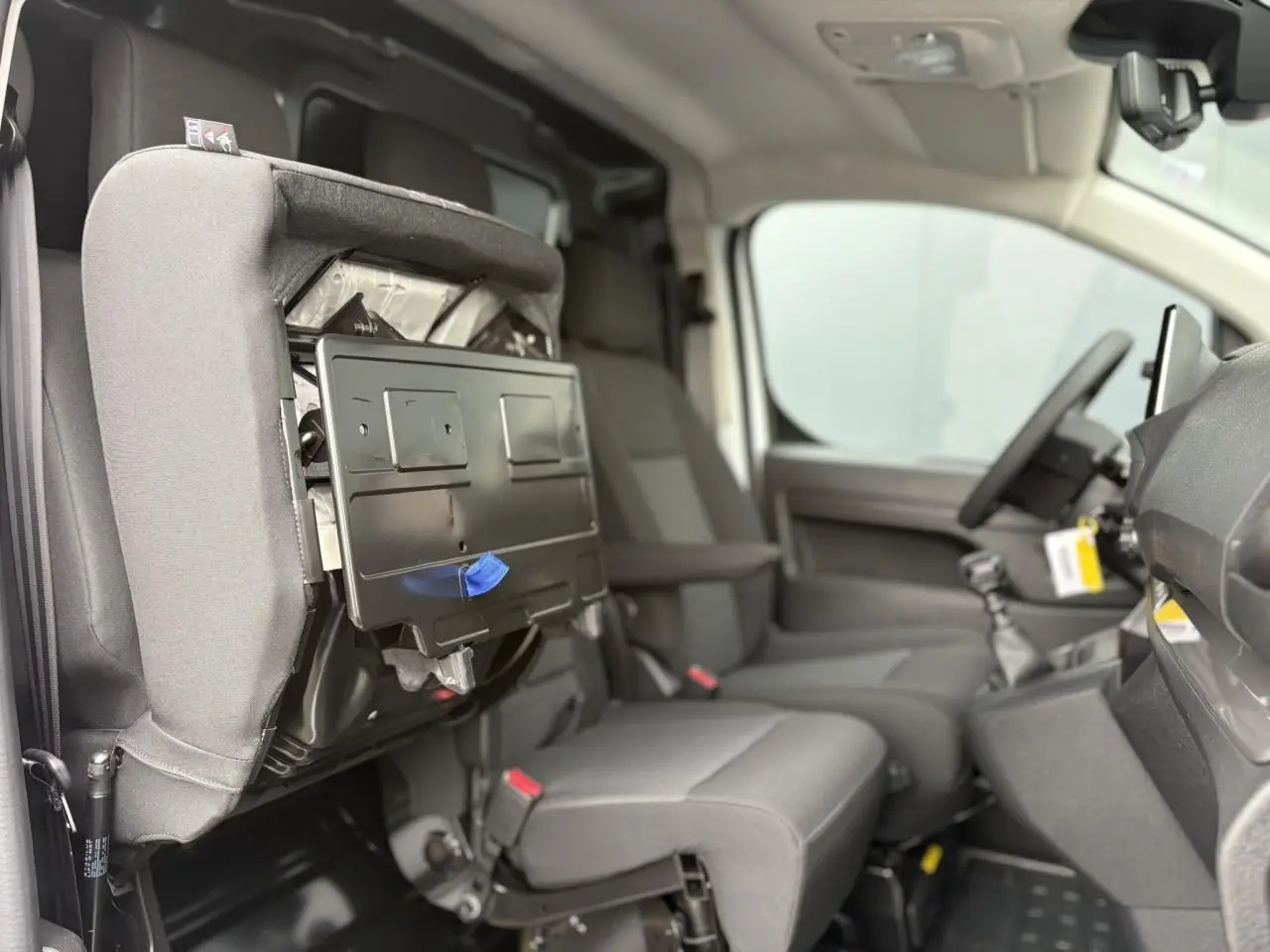 Vue intérieure côté droit du Peugeot Expert Fourgon 2025 montrant la banquette passager relevée et sièges en tissu bi-ton gris.