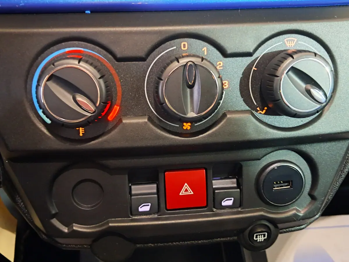 Gros plan sur la console centrale de l'AIXAM AMBITION 2025 bleu, montrant les commandes de climatisation et boutons de sécurité.