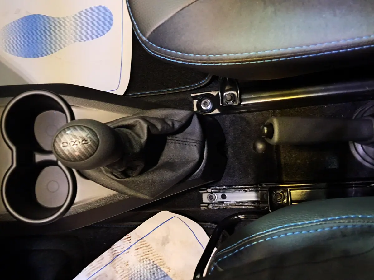 Gros plan sur la console centrale noire avec levier de vitesse et frein à main, sièges gris avec surpiqûres bleues visibles