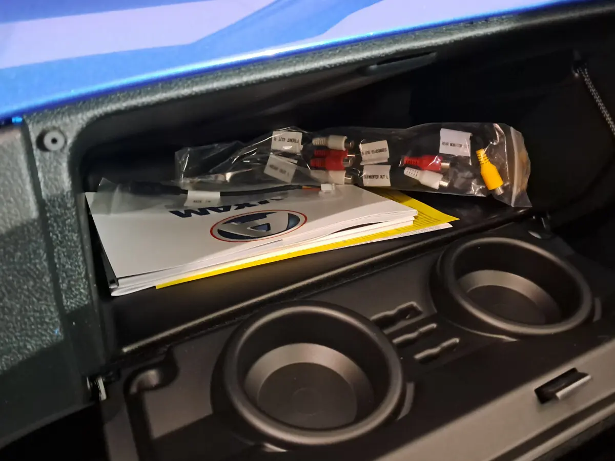 Coffre ouvert de l'AIXAM AMBITION bleu 2025 montrant des manuels et câbles, avec porte-gobelets intégrés.