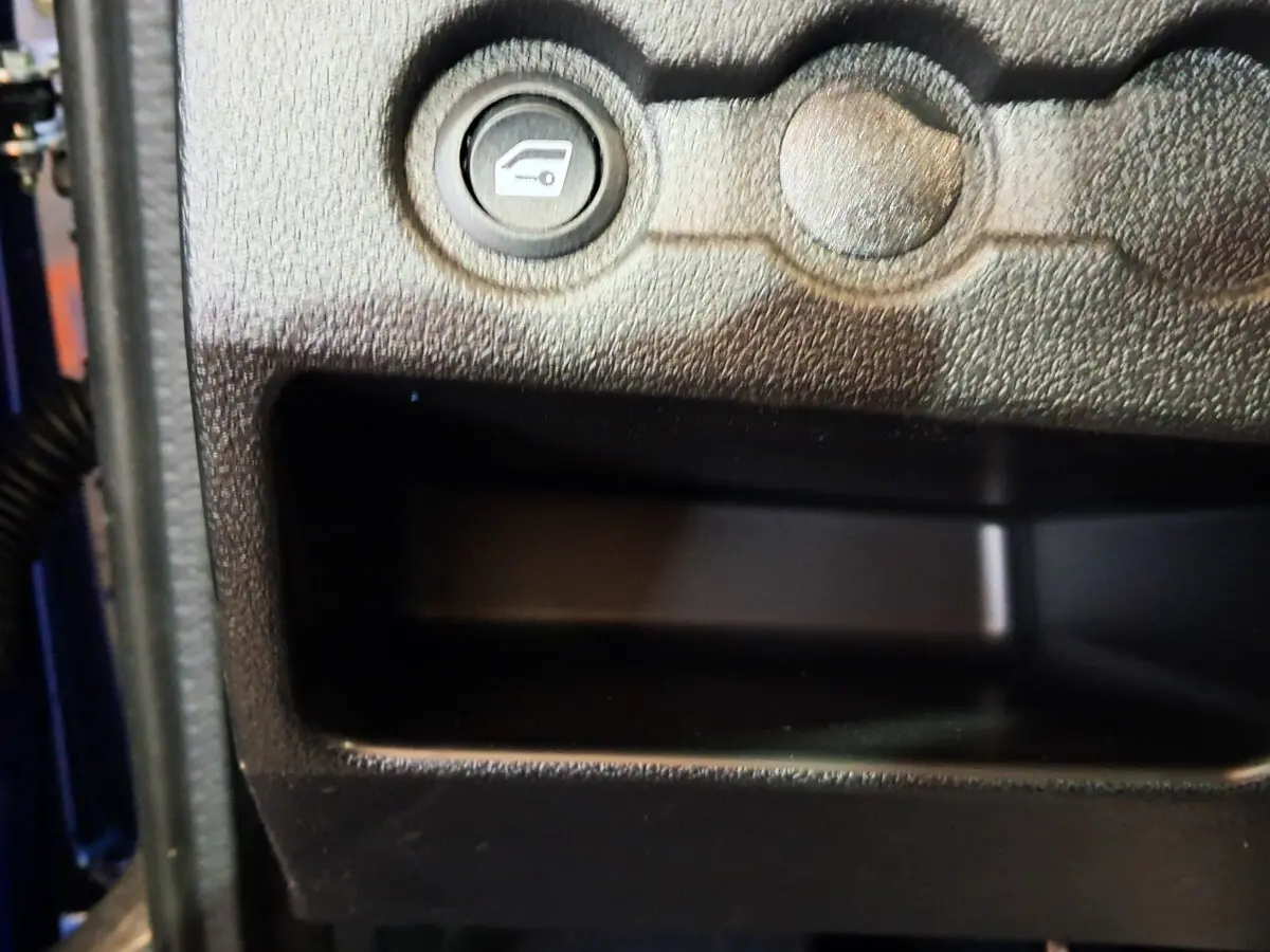 Gros plan sur le bouton d'ouverture du coffre dans l'habitacle d'une Aixam Ambition bleu 2025 côté conducteur.