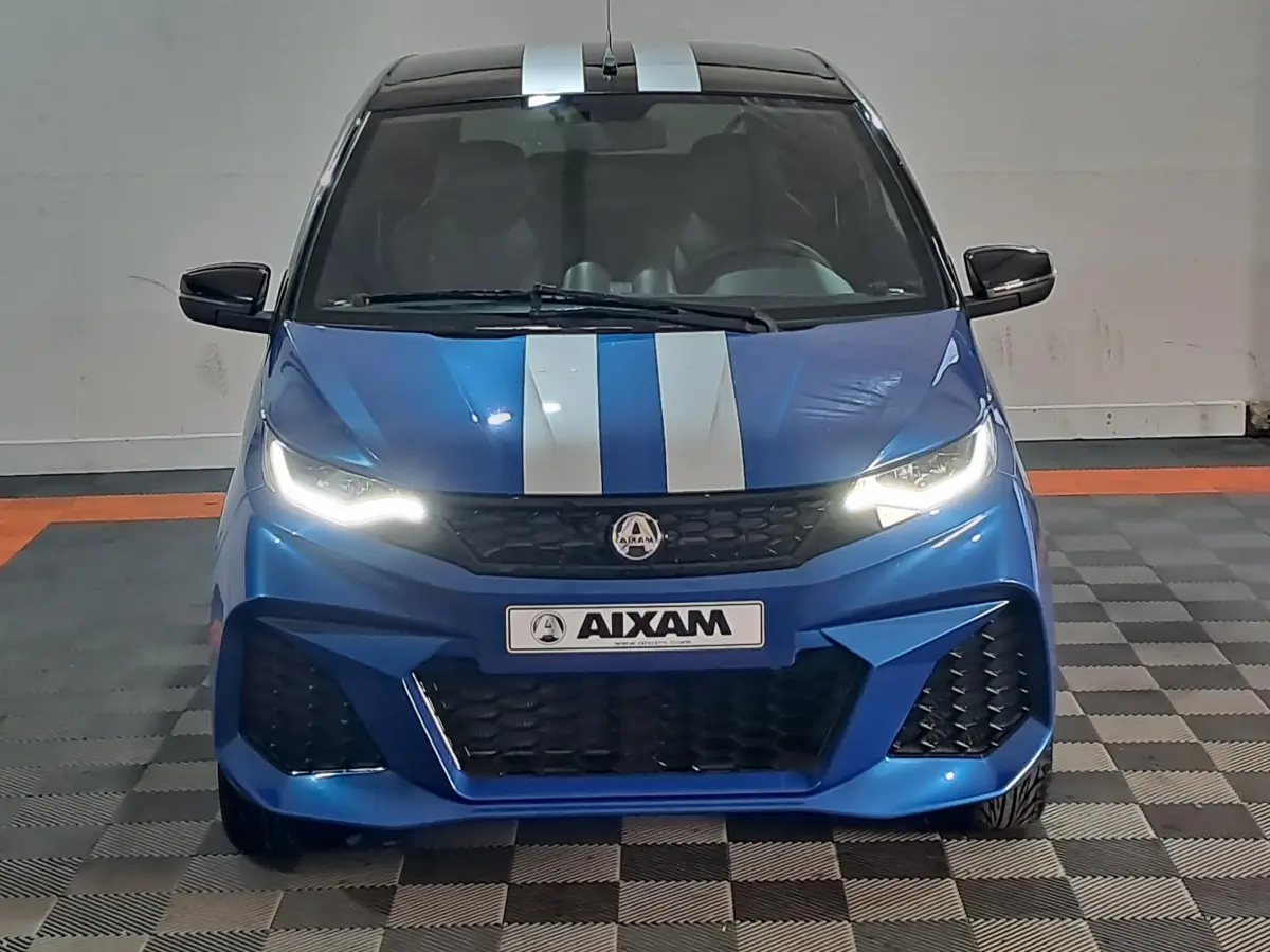 Vue frontale d'une Aixam Ambition 0.5 City GTO bleue avec bandes blanches et phares allumés dans un garage.