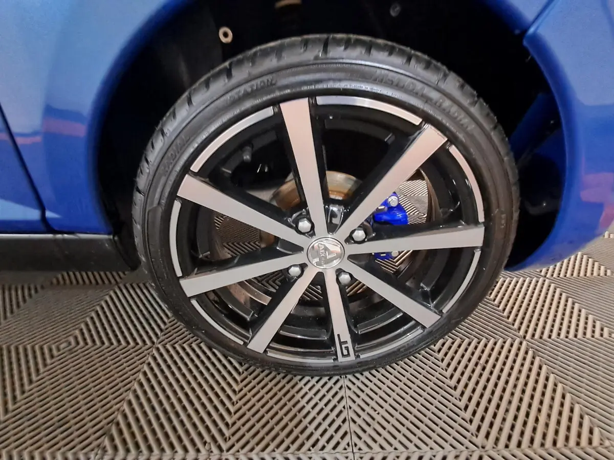 Gros plan sur la roue avant droite noire et argentée d'une AIXAM AMBITION bleu 2025 avec étrier de frein bleu visible.