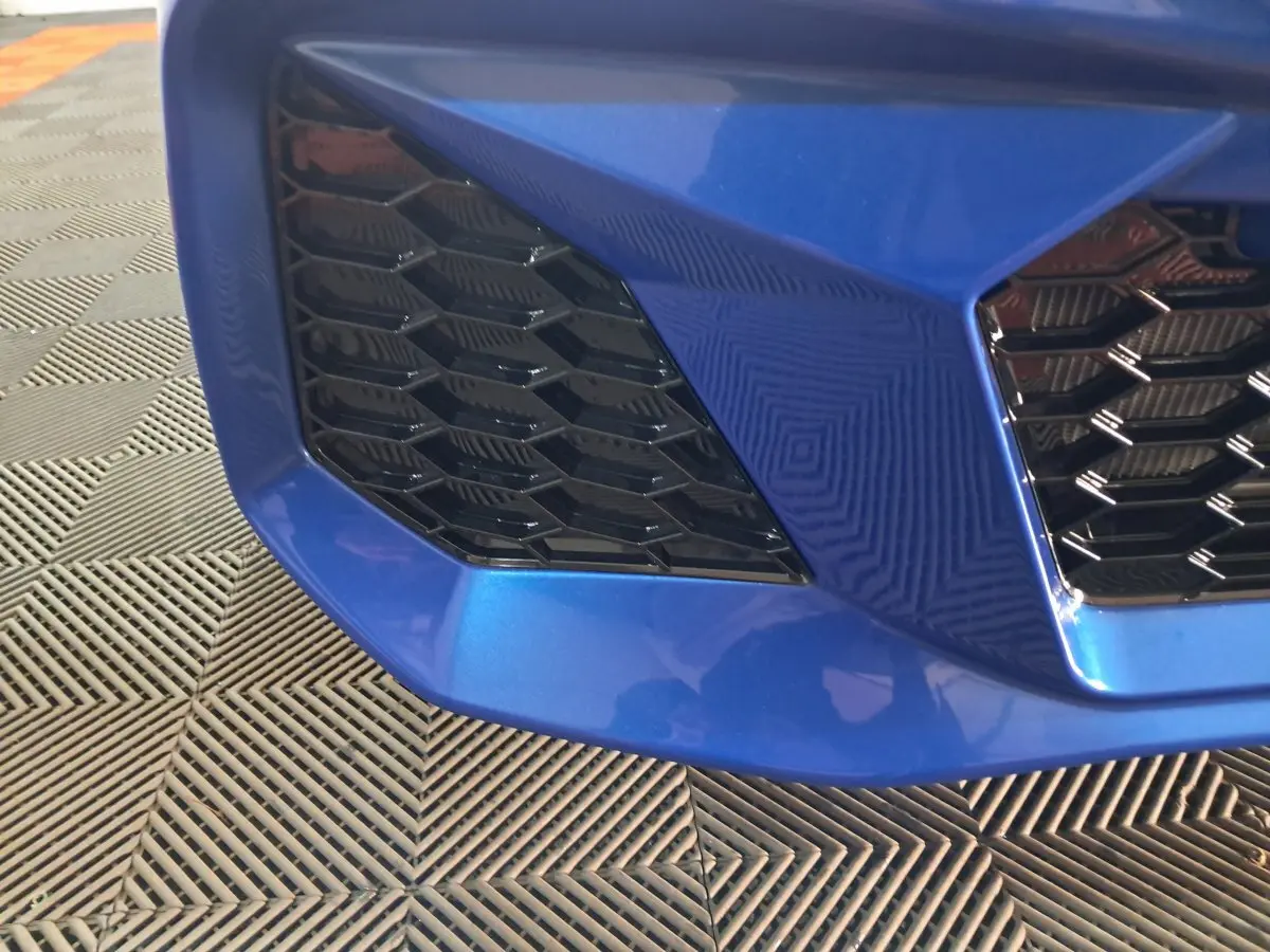 Gros plan sur la calandre avant gauche bleu métallisé de l'AIXAM AMBITION 0.5 CITY GTO 2025 avec grille noire hexagonale.