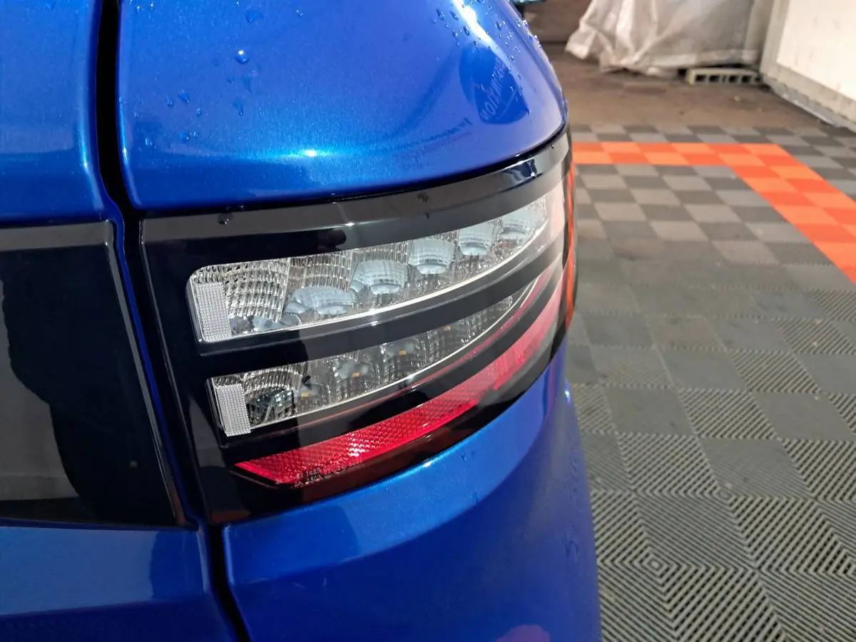 Gros plan sur le feu arrière droit bleu métallisé de l'AIXAM AMBITION 0.5 CITY GTO 2025 dans un garage.