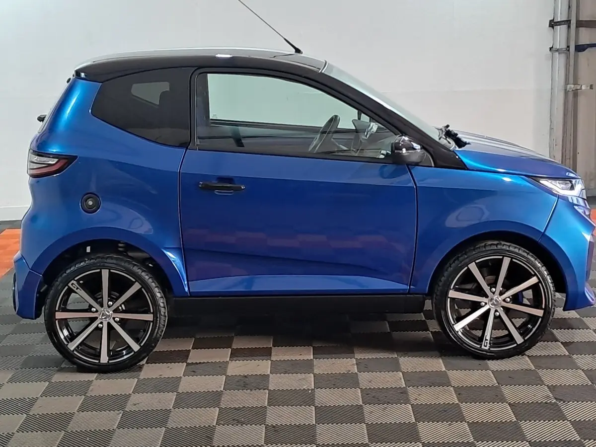 Profil côté gauche d'une Aixam Ambition 0.5 City GTO bleu 2025 avec jantes noires et rétroviseur caméra au conducteur.
