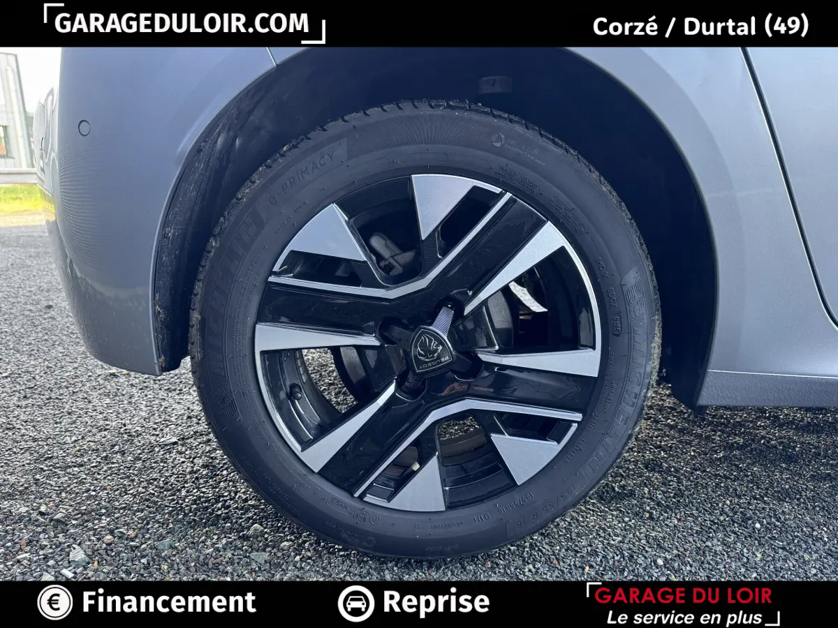 Gros plan sur la roue avant droite d'une Peugeot 208 Hybrid gris clair avec jante alliage noire et argentée.