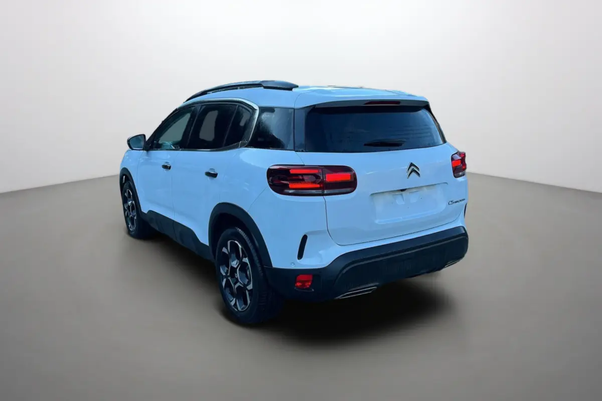 Vue 3/4 arrière droite d'un Citroën C5 Aircross blanc okénite avec barres de toit et vitres surteintées.