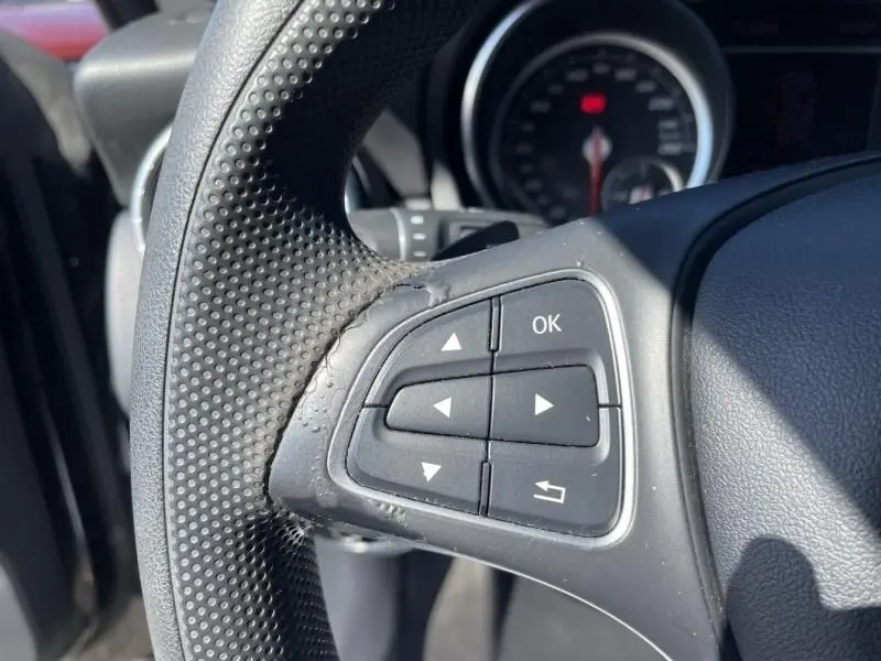Gros plan sur les commandes au volant à gauche du Mercedes Classe CLA Shooting Brake noir, avec le compteur en arrière-plan flou.