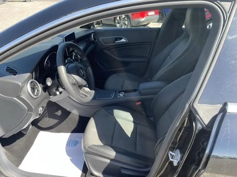 Vue intérieure côté conducteur de la Mercedes Classe CLA Shooting Brake noire, avec tableau de bord et sièges en tissu gris.