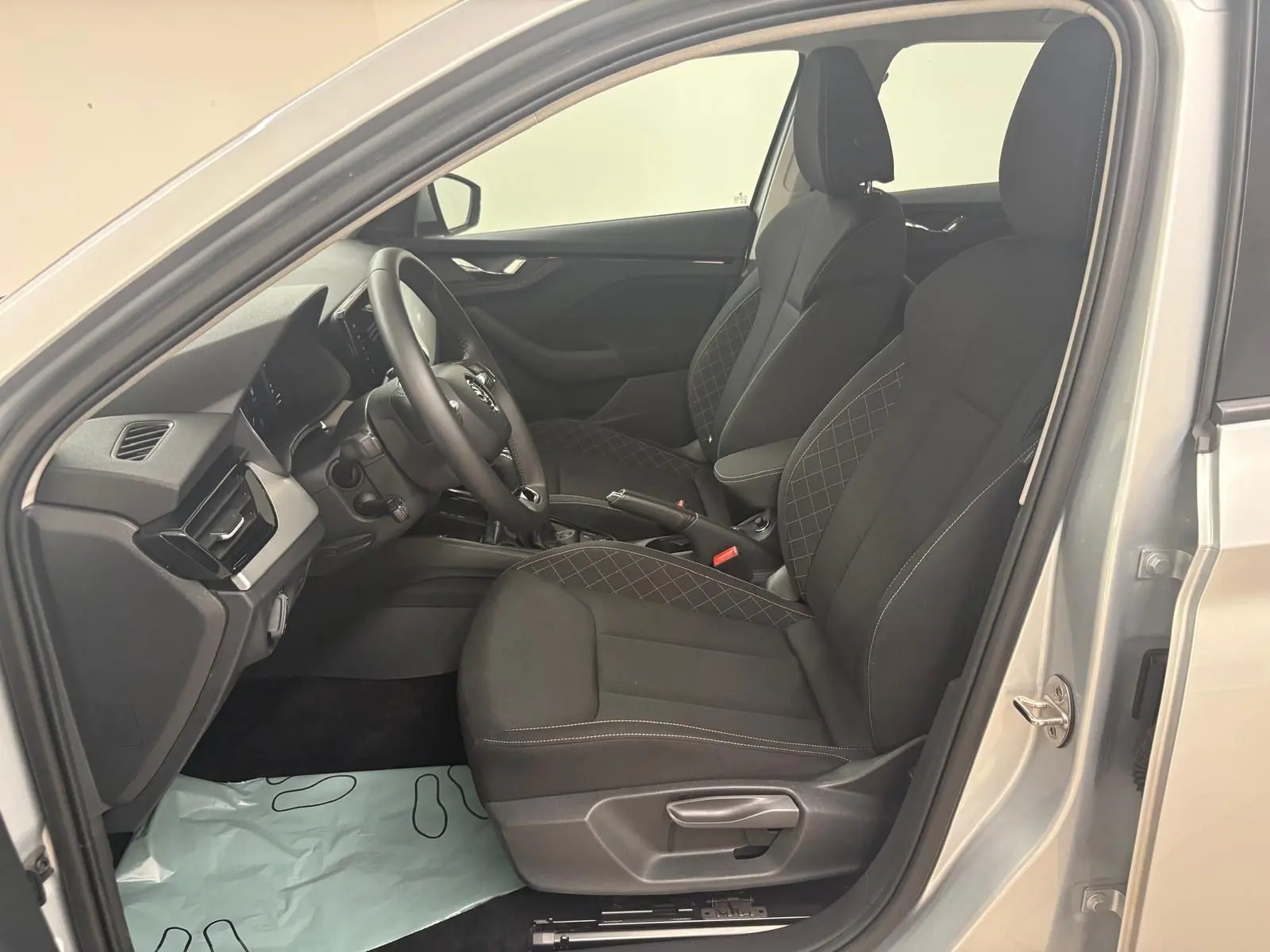 Vue intérieure côté conducteur de la Skoda Scala gris argent 2024, sièges tissu noir avec surpiqûres contrastées.