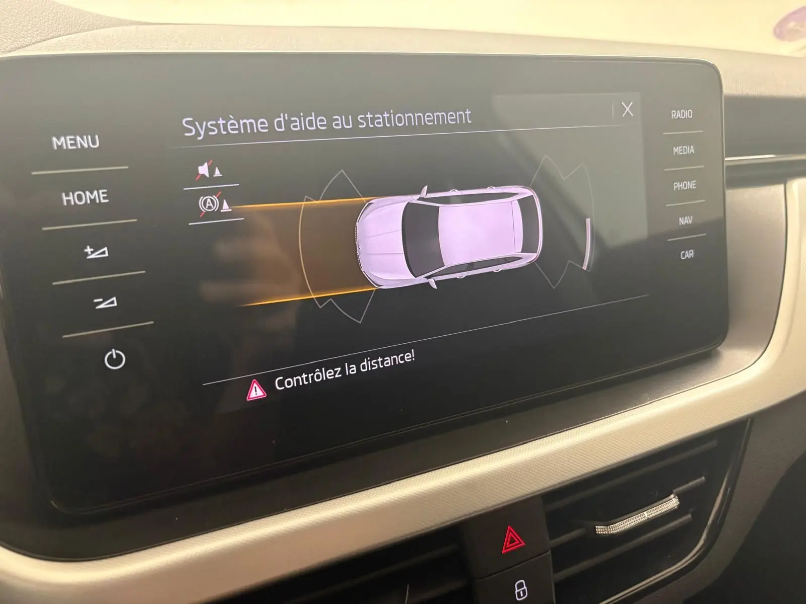 Écran central du Skoda Scala 2024 montrant le système d'aide au stationnement avec vue de dessus du véhicule gris argent.