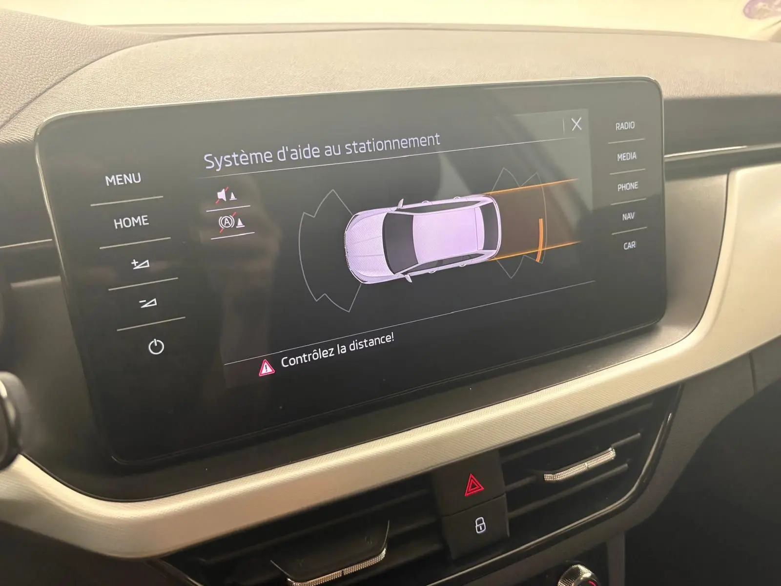 Écran central du Skoda Scala 2024 affichant le système d'aide au stationnement avec vue schématique du véhicule gris argent.