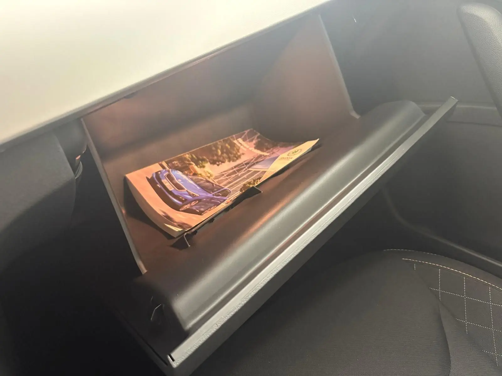 Vue intérieure du coffre à gants ouvert d'une Skoda Scala 2024, montrant une brochure avec une voiture bleue.