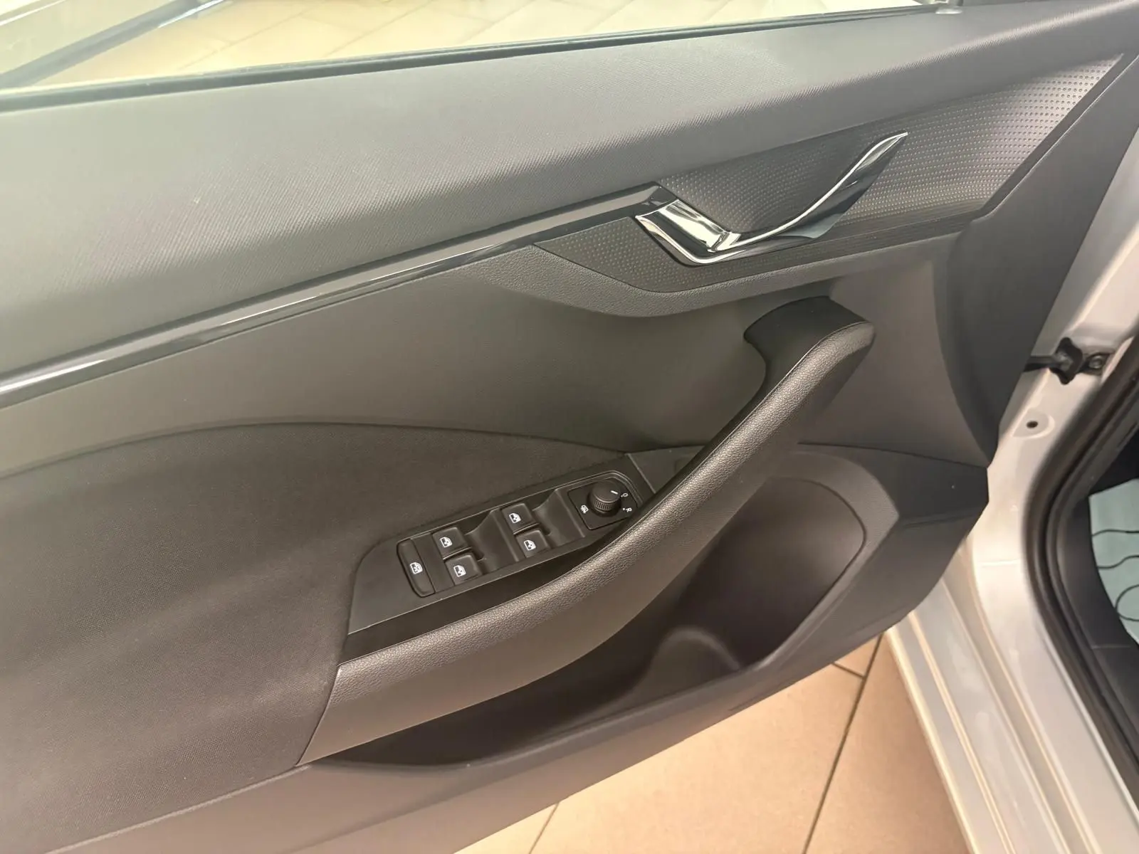 Vue intérieure côté conducteur de la porte d'une Skoda Scala gris argent 2024 avec commandes électriques des vitres et poignée chromée.