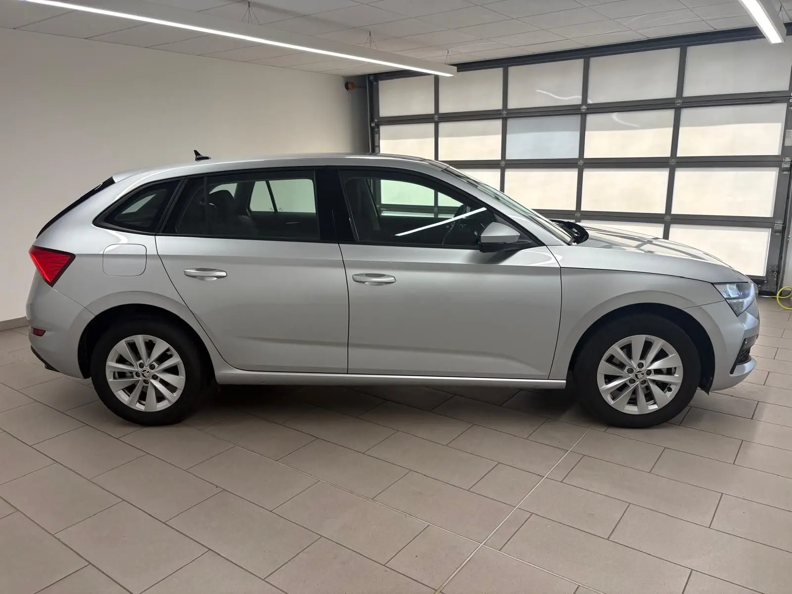 Vue de profil côté gauche d'une Skoda Scala gris argent 2024 en version 1.0 TSI 110 DSG7 Business stationnée en intérieur.