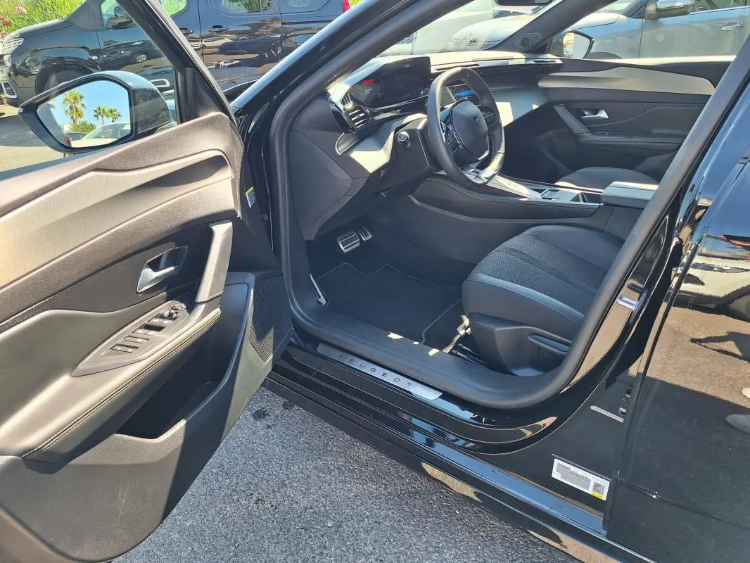 Intérieur côté conducteur d'une Peugeot 308 SW Hybrid noir, avec porte ouverte et cockpit numérique visible.