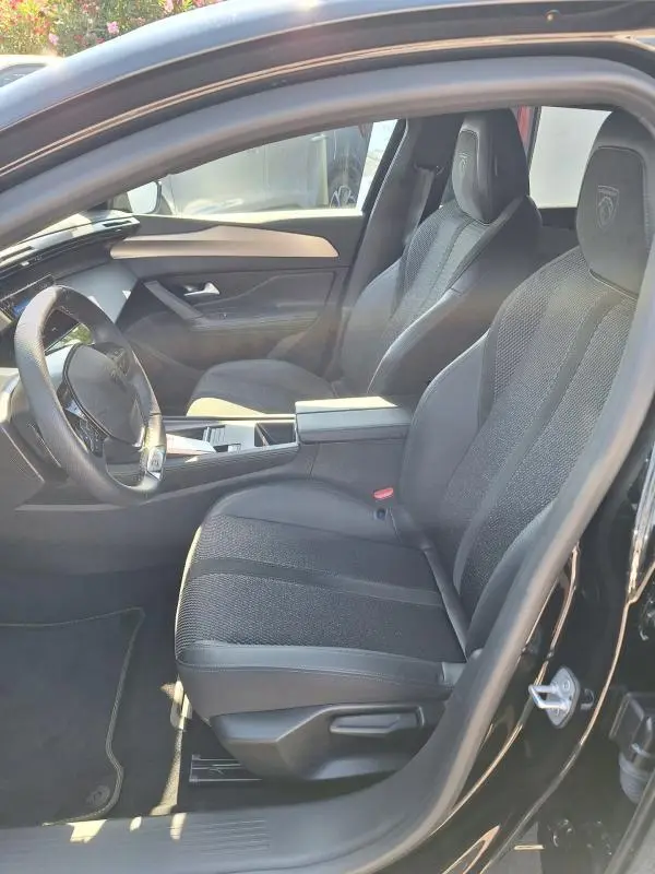 Vue intérieure côté conducteur du Peugeot 308 SW Hybrid 145 e-DCS6 GT 2025 noir, sièges sport avec logo embossé et cockpit numérique.