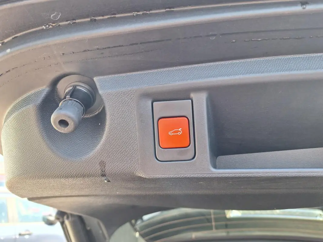 Gros plan sur le bouton rouge d'ouverture électrique du hayon du Peugeot 308 SW Hybrid noir, vue intérieure arrière.