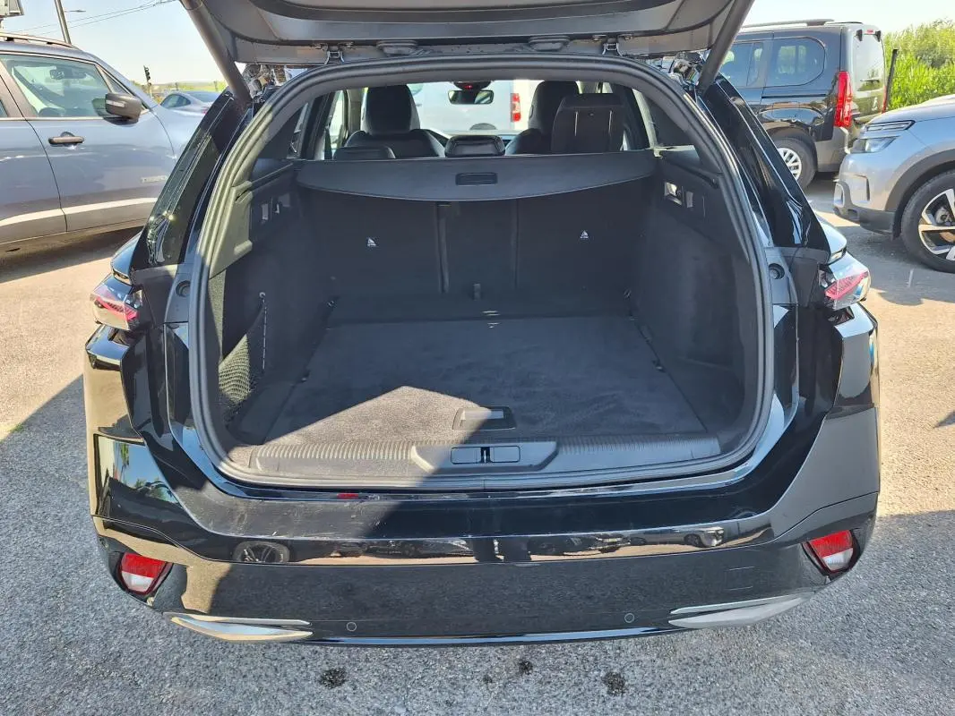 Coffre ouvert en vue arrière d’un Peugeot 308 SW Hybrid 145 noir, montrant un espace de chargement spacieux et propre.