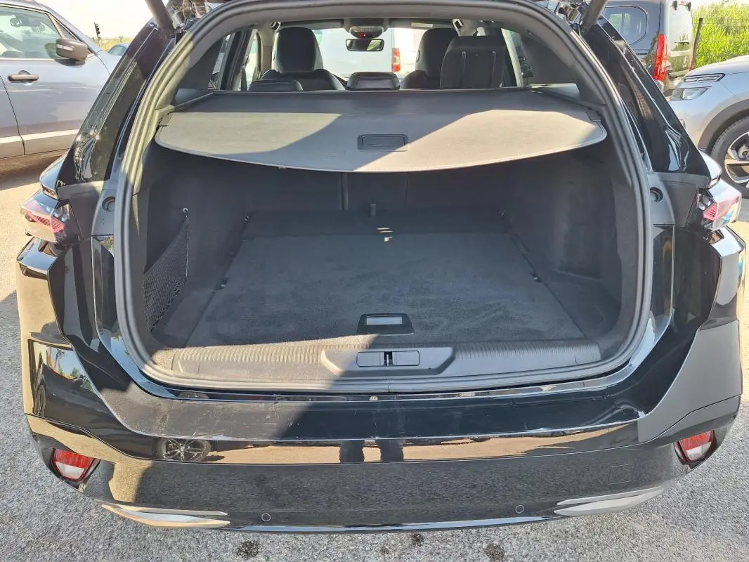 Coffre ouvert de la Peugeot 308 SW Hybrid 145 e-DCS6 GT noir, vue arrière montrant l’espace de chargement et la plage arrière.