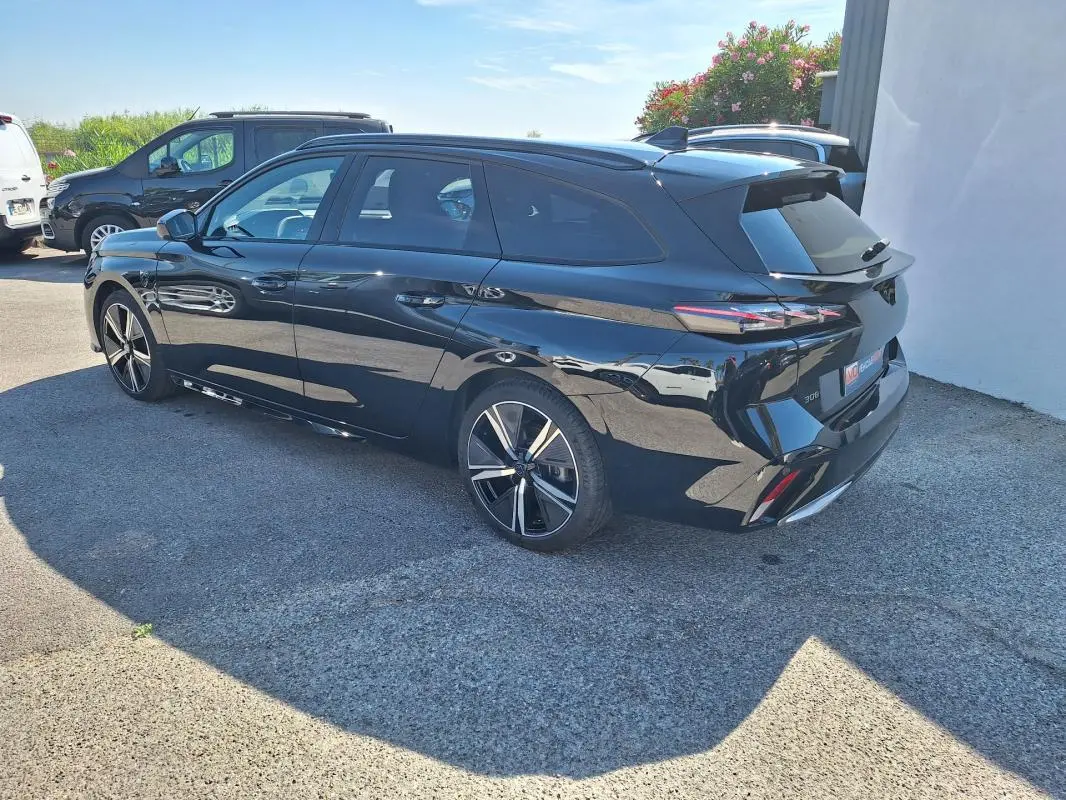 Peugeot 308 SW Hybrid noir vue 3/4 arrière droit, avec barres de toit et jantes alliage 18 pouces.