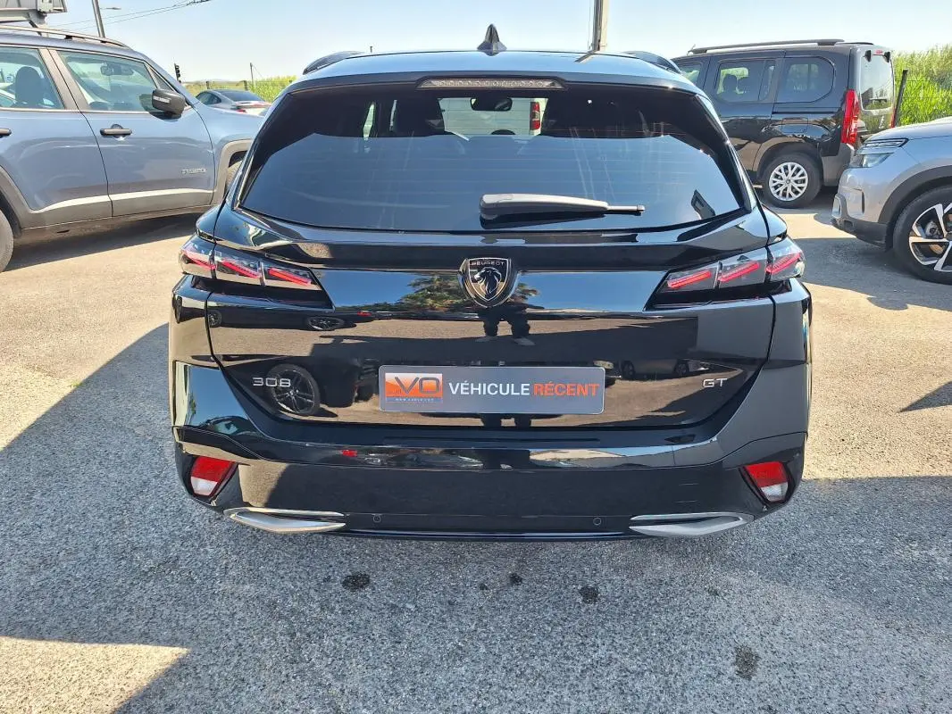 Vue arrière d’un Peugeot 308 SW Hybrid 145 e-DCS6 GT noir avec barres de toit et feux LED distinctifs.