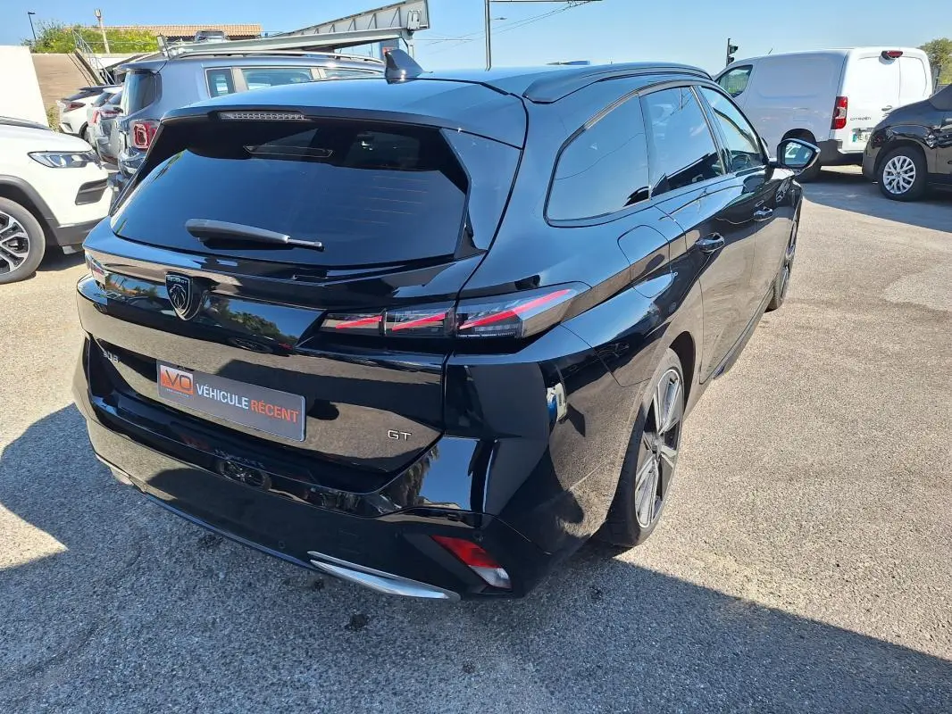 Vue 3/4 arrière droite d'une Peugeot 308 SW Hybrid 145 GT noire avec barres de toit et jantes alliage 18 pouces.