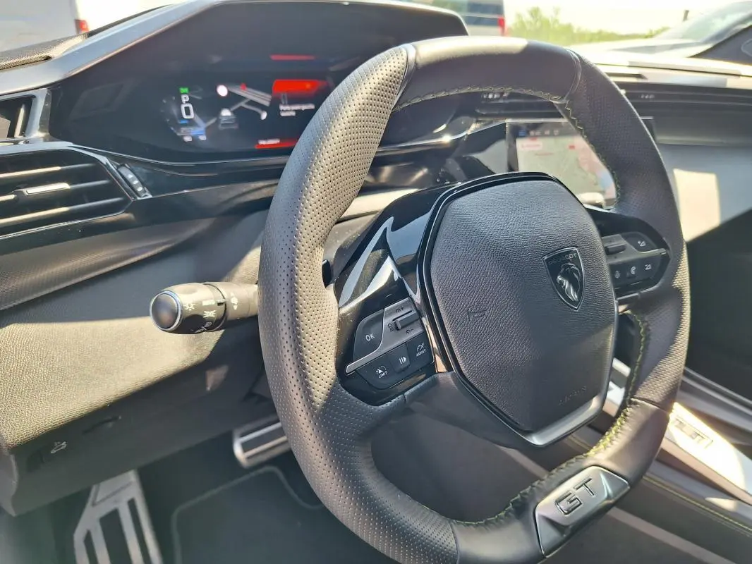 Vue intérieure rapprochée du volant GT en cuir perforé et du cockpit numérique de la Peugeot 308 SW Hybrid 145 noir.