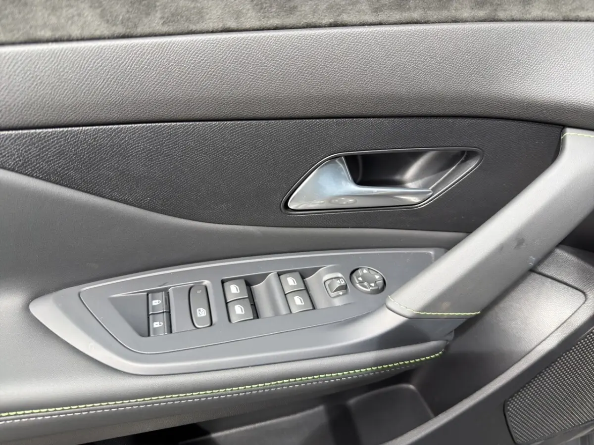 Gros plan sur la porte intérieure côté conducteur de la Peugeot 308 gris clair, avec commandes électriques et surpiqûres vertes.