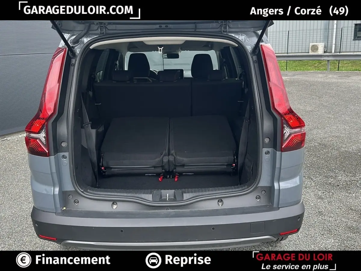 Vue arrière du coffre ouvert d’un Dacia Jogger gris, montrant les sièges arrière rabattus et les feux arrière rouges.