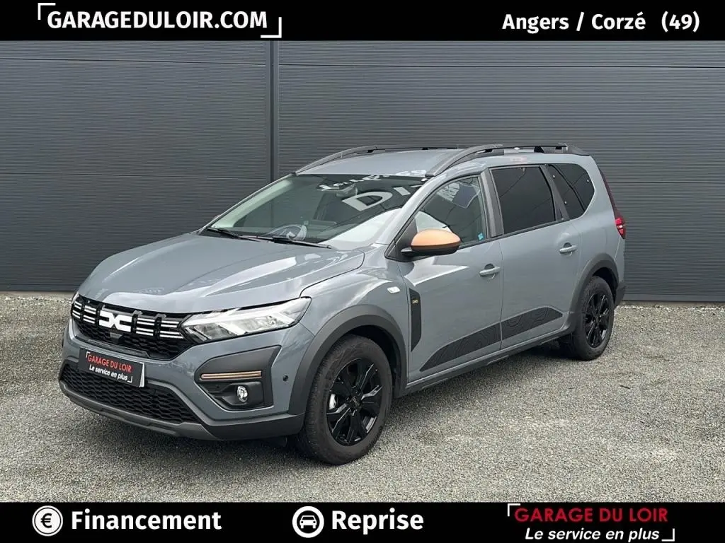 Vue 3/4 avant d’un Dacia Jogger Extreme+ Hybrid 140 gris avec rétroviseur couleur cuivre et jantes noires.